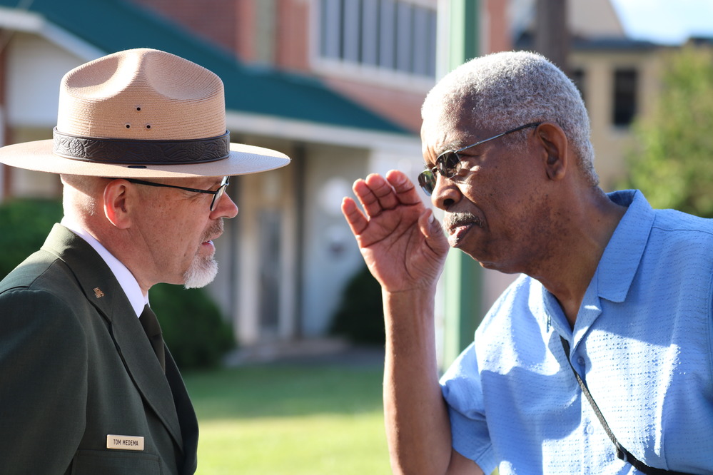 NPS Park ranger on left speaking with man with hand shielding sun from eyes; both seen from chest up