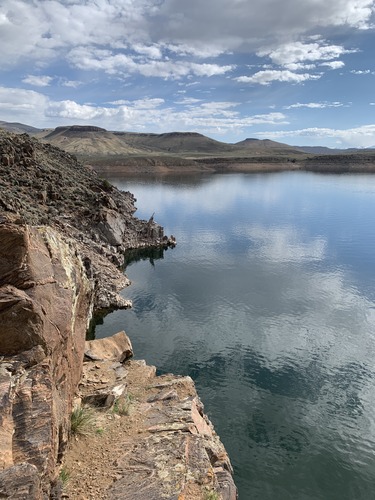 Steep, rocky cliffs next to a large body of water. Brownish-green mesas are in the background