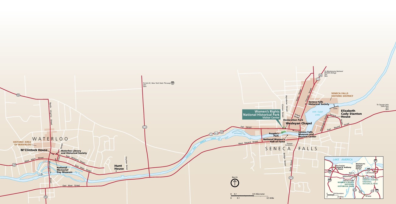 Map of Women’s Rights National Historical Park in New York. The park’s visitor center is above the Cayuga and Senegal Canal, in Seneca Falls, which runs horizontally across the map. Notable sites are labeled here and in Waterloo, west of Seneca Falls along the blue canal. Roads are bright red, and the area is beige. A small area map can also be found in the bottom right. 