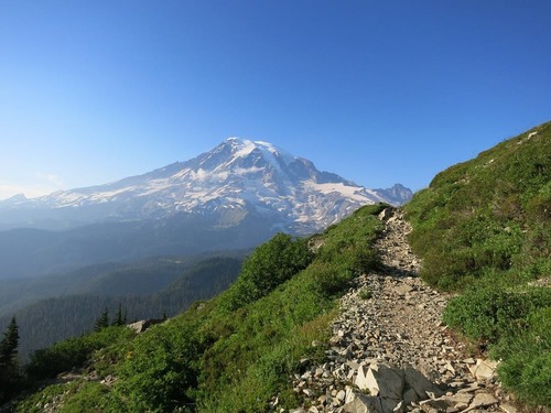 A narrow rocky trail along a steep slope heading towards a glaciated mountain peak. 