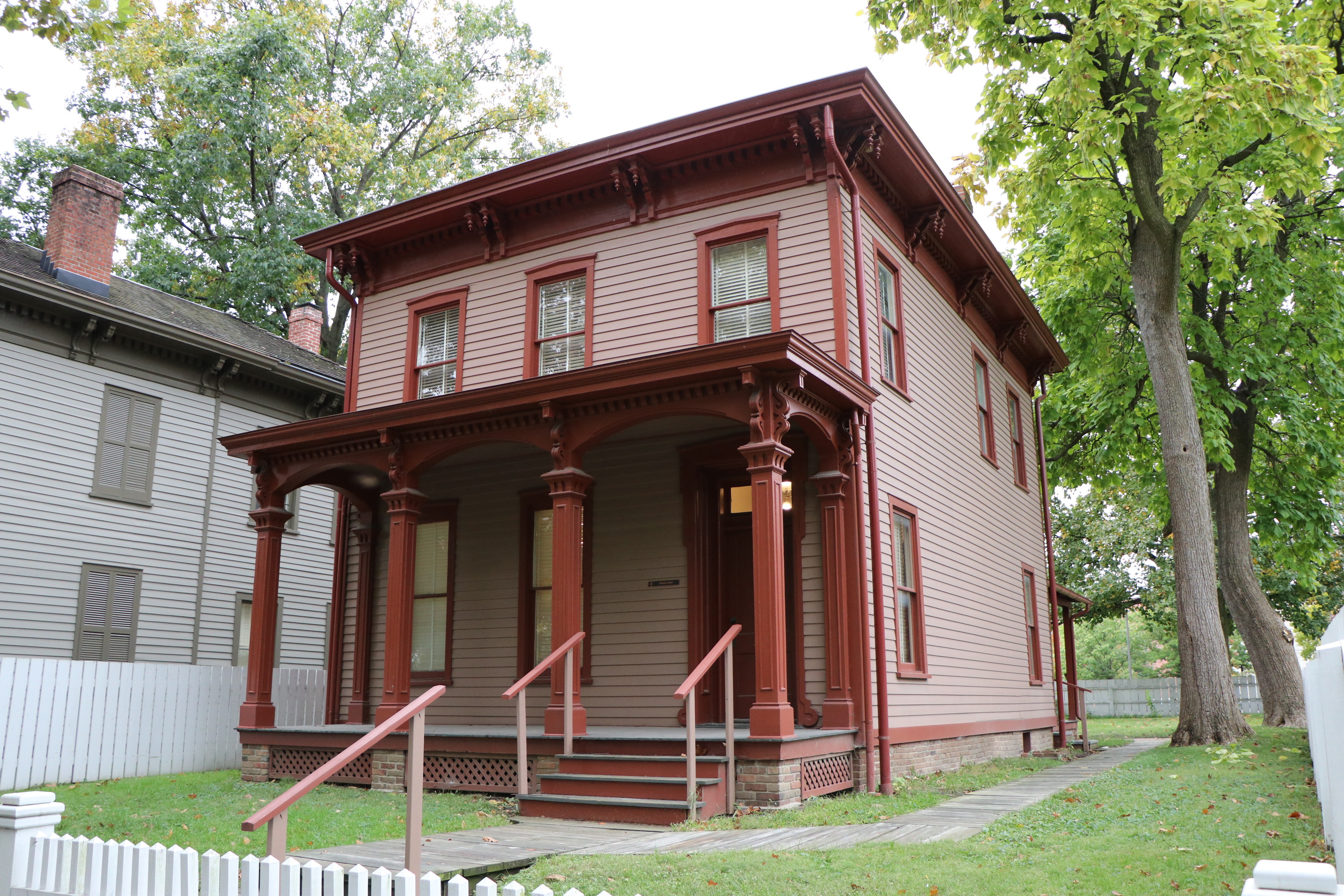 A two-story light red house with darker red accents and a fenced-in yard.