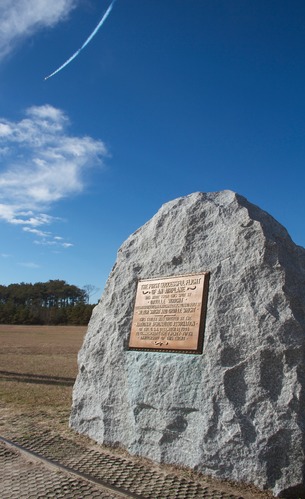 A plane flies over the First Flight Boulder
