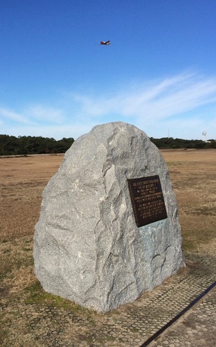 A plane flies over the First Flight Boulder
