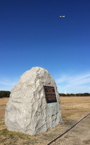 A plane flies over the First Flight Boulder