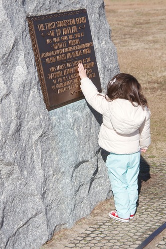 A young girl touches the plaque on the First Flight Boulder