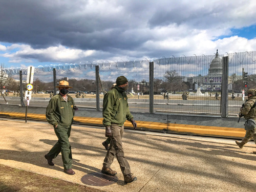 Several National Park Service employees walking next to a fence with the U.S. Capitol building in the background 