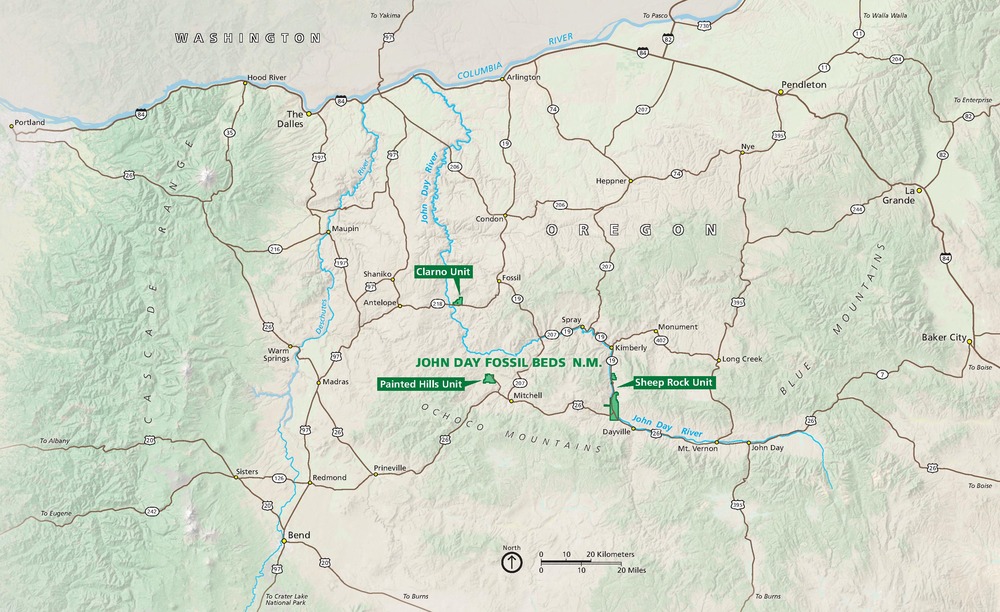 Map of John Day Fossil Beds National Monument in Oregon. Three units are shown as small bright green shapes above the Ochoco Mountains and east of the Cascade Range. Mountainous areas are pale mint green and surrounding areas are bone white. Rivers are blue.