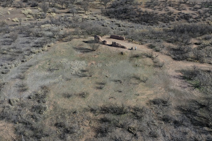 aerial photo taken from oblique angle depicting two figures near earthen ruins on a slightly raised circular area