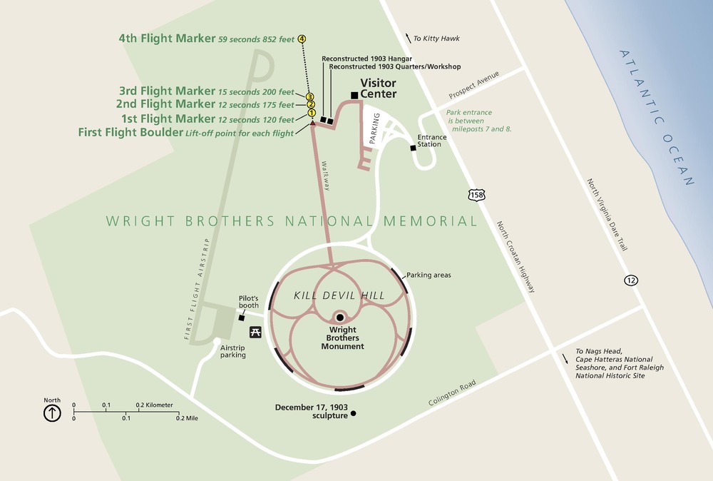 Map of Wright Brothers National Memorial in North Carolina. The park area is shaded green and shaped like a fat bowtie. The monument is at the center of a winding walkway shaped like an orchid bloom. A blue triangle of the Atlantic Ocean juts down, covering the map’s top right corner.