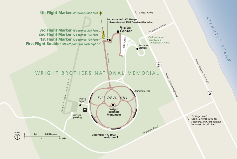 Map of Wright Brothers National Memorial in North Carolina. The park area is shaded green and shaped like a fat bowtie. The monument is at the center of a winding walkway shaped like an orchid bloom. A blue triangle of the Atlantic Ocean juts down, covering the map’s top right corner.
