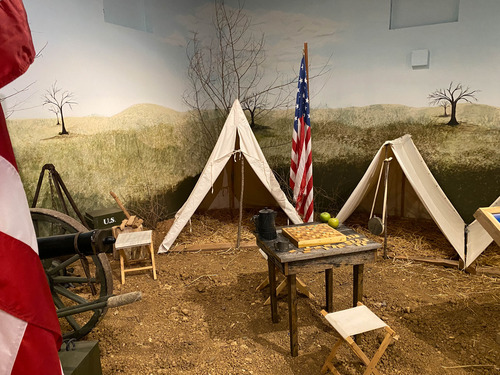 Museum exhibit of Ciril War soldier camps including two tents, a cannon, a desk, foldable seats, and U.S. flags