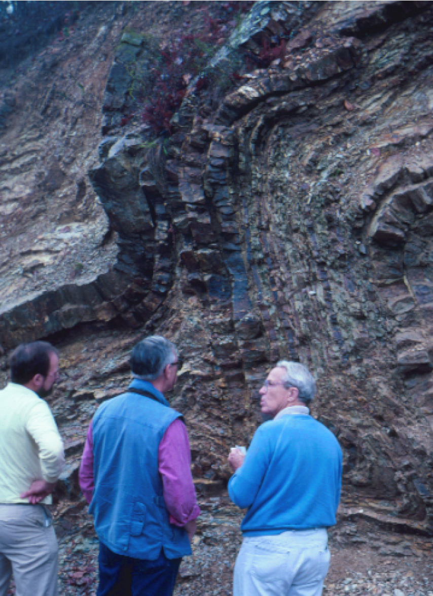 three people standing in front of rock cliff with folded rock layers