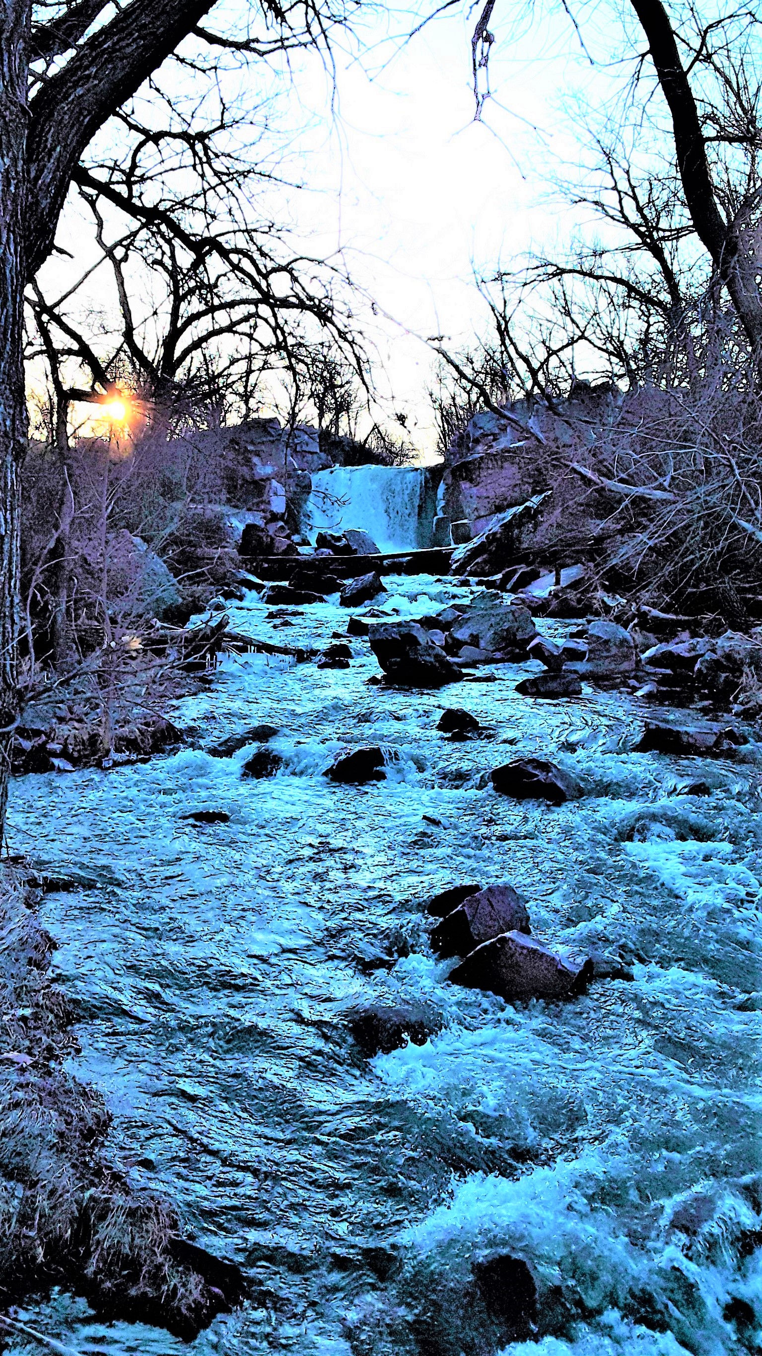 Waterfall flowing into rock-strewn creek and the sun rising in the background