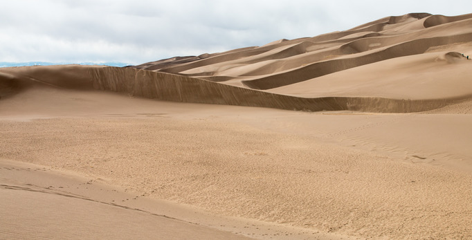 The sun shines on some of the smaller sand dunes that lead into the large dune in the dune field. 