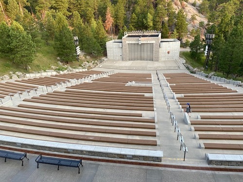 View from the top of the amphitheater seating at the bottom of the image with the stage and amphitheater building at the top of the image.