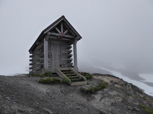 A small wooden cabin sits on a rocky outcrop with stairs leading up to it. 