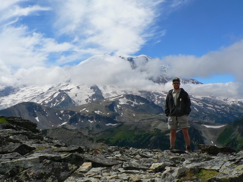 A volunteer stands on a ridge looking at the view of Mount Rainier.