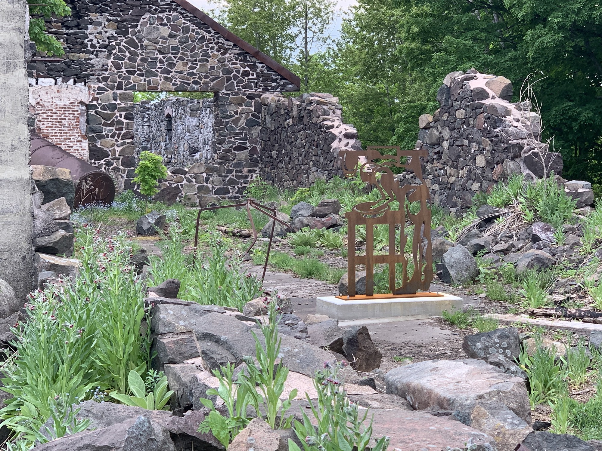 Standing in the middle of rubble from an old mining building with no roof is a sculpture of a man bent over a basin washing up. 
