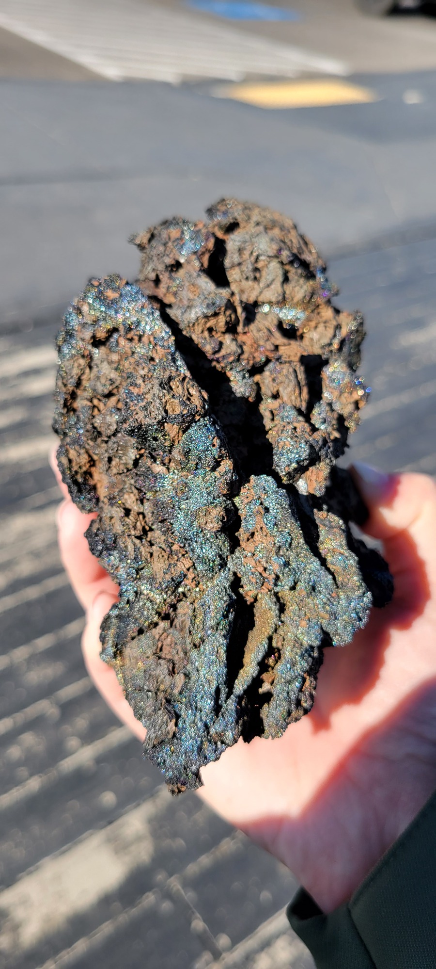a rock larger than the hand holding it with many bands of a blue, shiny glaze