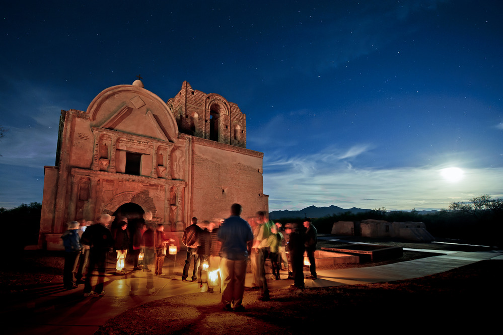 group of visitors with candle lanterns in front of church with full moon in background