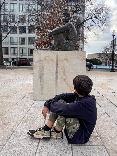 Kid mimicking a statue of Dwight D. Eisenhower as a sitting with his arms and legs crossed