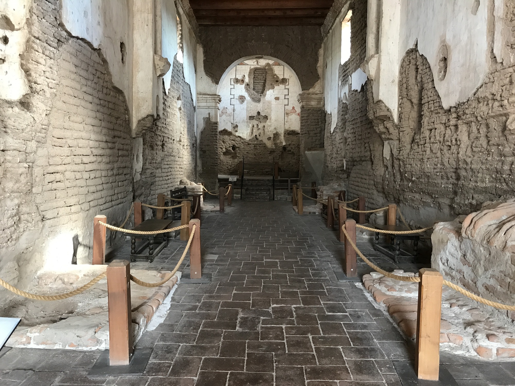 long nave with benches and roped-off side altar remnants, no flowered cross over altar