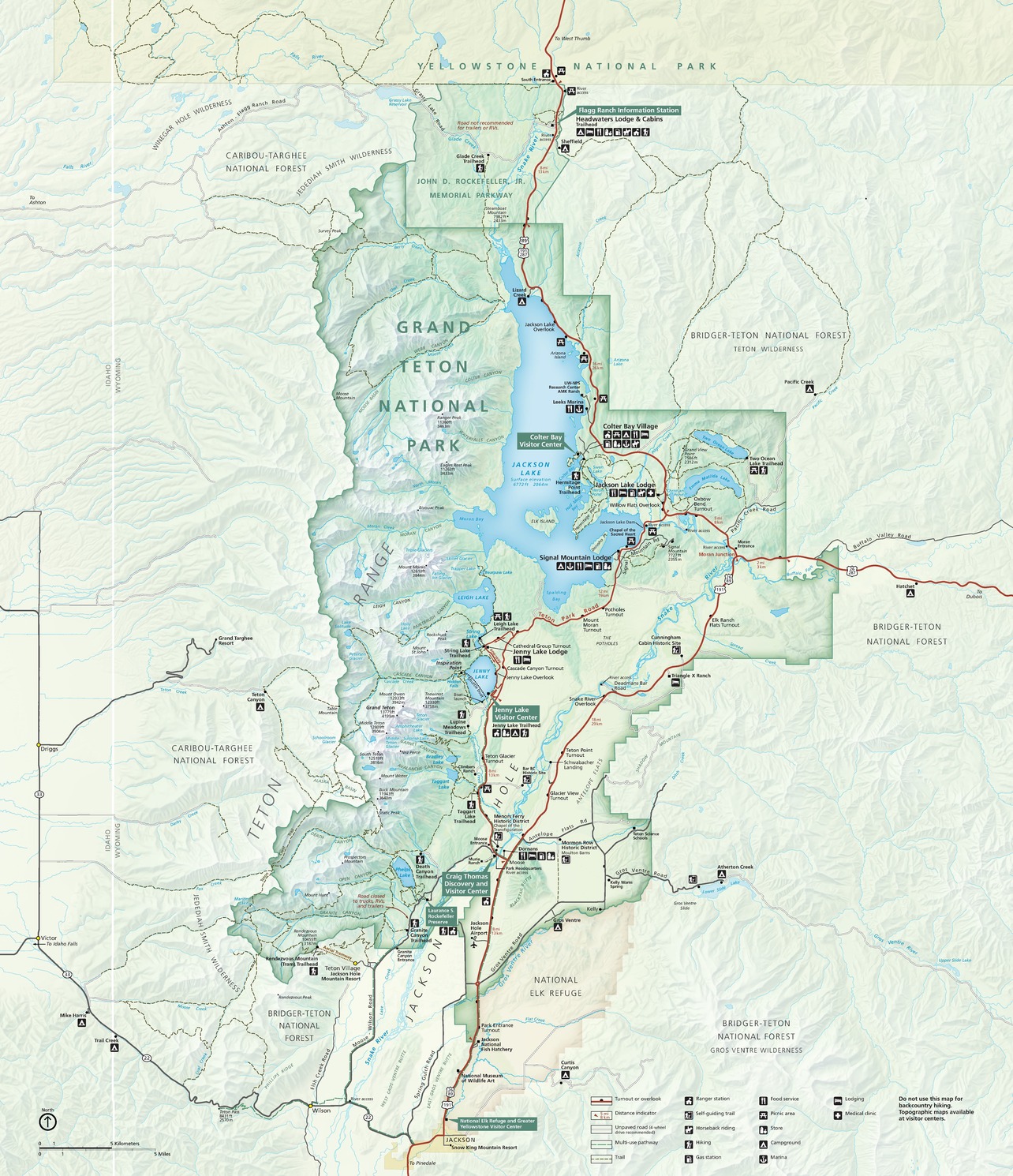 A map of Grand Teton National Park in Wyoming. The park is shown primarily in a saturated green color; within the park, its mountain peaks are depicted in snowy white; its lowlands in a yellowish-beige; its interspersed lakes in blue; and its major roads and highways in red.