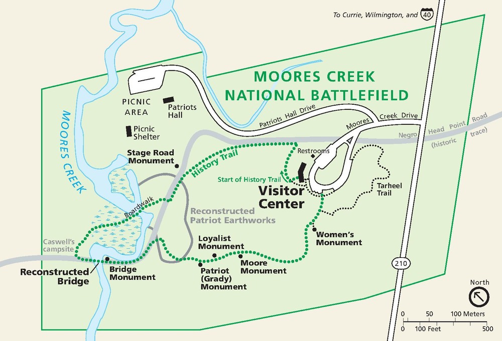 Park map of Moores Creek National Battlefield in North Carolina. The park is outlined and shaded green, and the surrounding area is tan. Green dotted and black dotted lines represent trails.