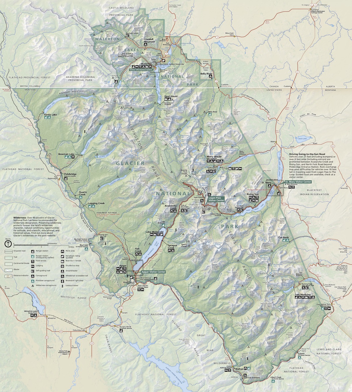 Map of Glacier National Park in Montana. Shown in sage green as a roughly trapezoidal area, the park stretches diagonally from the northwest to the southeast through the center of the map region, with a small and craggy appendage of green extending even further north to encompass Waterton Lakes National Park in Alberta, Canada. Hundreds of beige glaciers and mountain ridges, powder blue waterways, color-coded campgrounds, brown roads, and other sites are labeled across the landscape.
