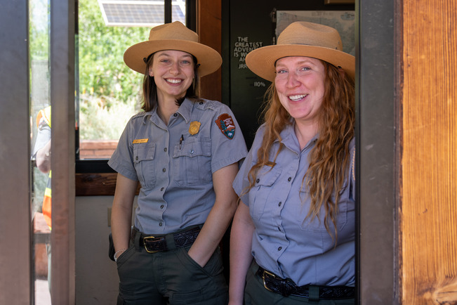 Two smiling fee rangers stand inside the fee booth and pose for a photo.