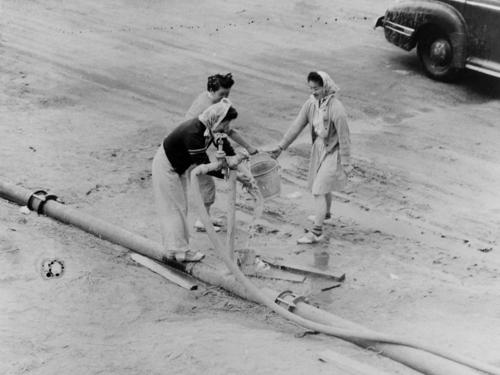 Relocation Nisei girls getting a bucket of water from one of the hydrants at the relocation center.