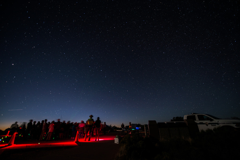 a group of people stands with red lights as stars fill the sky overhead