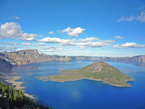 an island with trees in the middle of a large lake surrounded by rocky walls