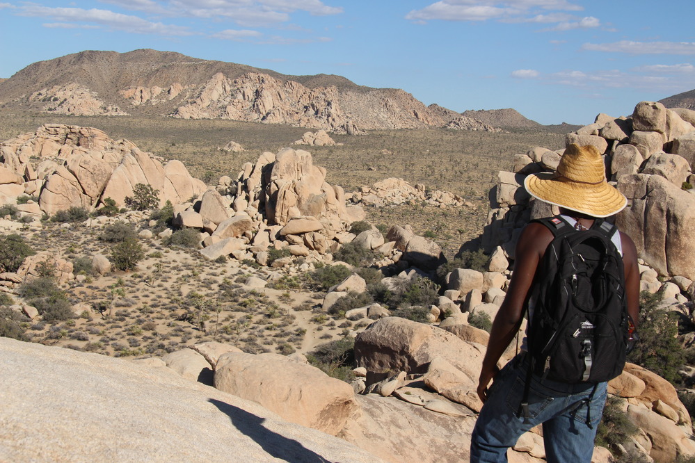 a hiker stands atop rocks, looking out over a desert valley
