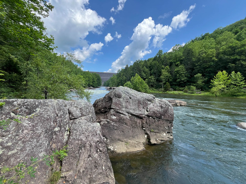 River with large boulders and lined with tree-covered ridges 