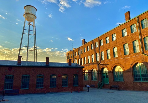Thomas Edison's Laboratory Courtyard. Rocky paved ground with red brick factory buildings, water tower and blue sky in the background.