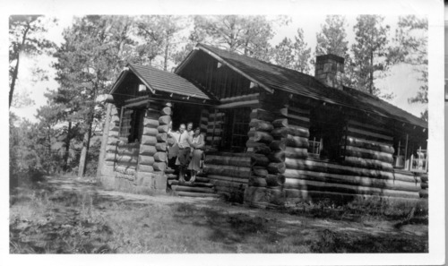 Historic photo of three people standing outside a log building