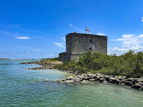Small two-story stone Spanish colonial fort on an island with a rocky shore and wetlands