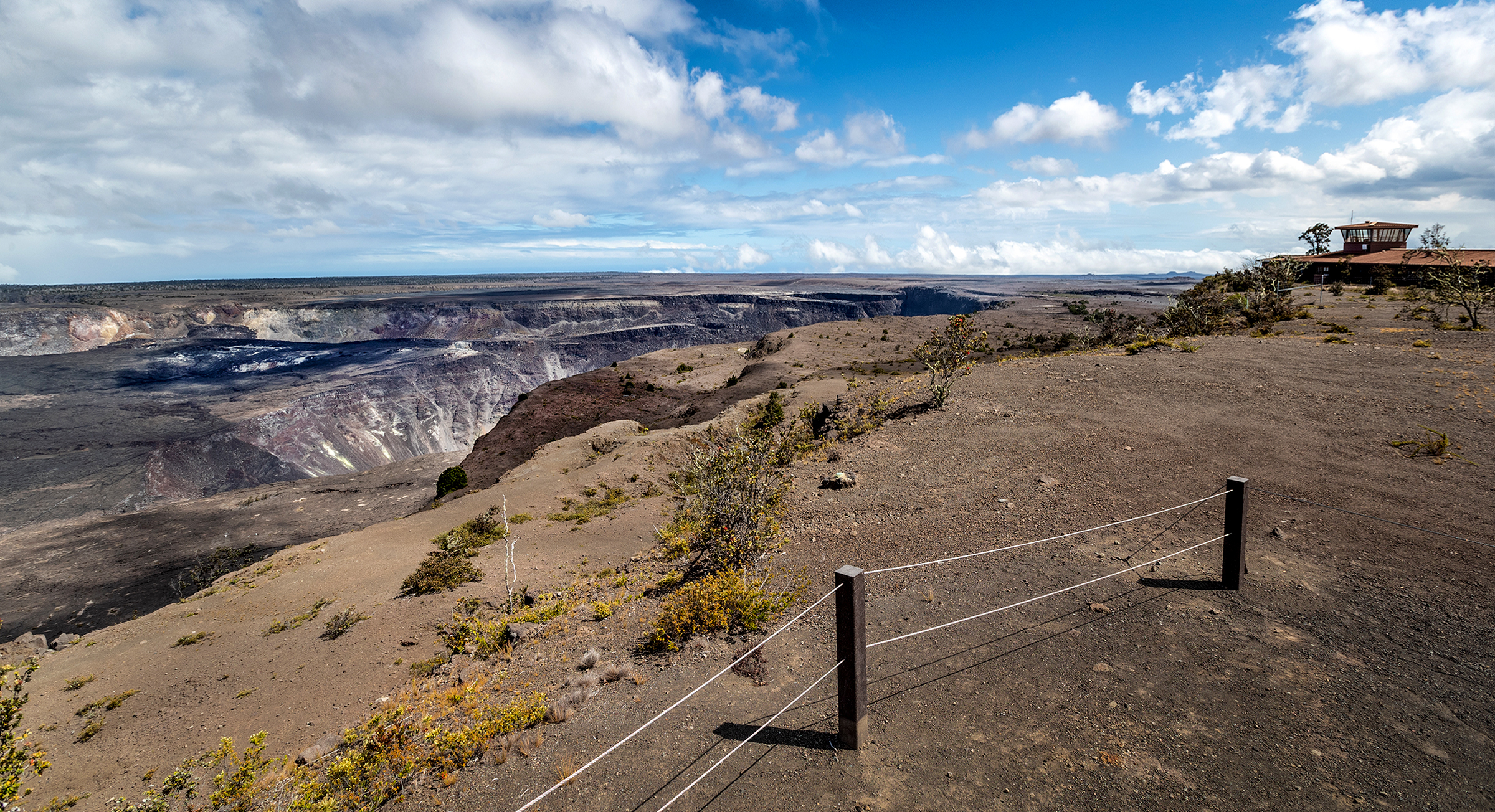 Post and cable barriers near the edge of a cliff with a building in the background. 