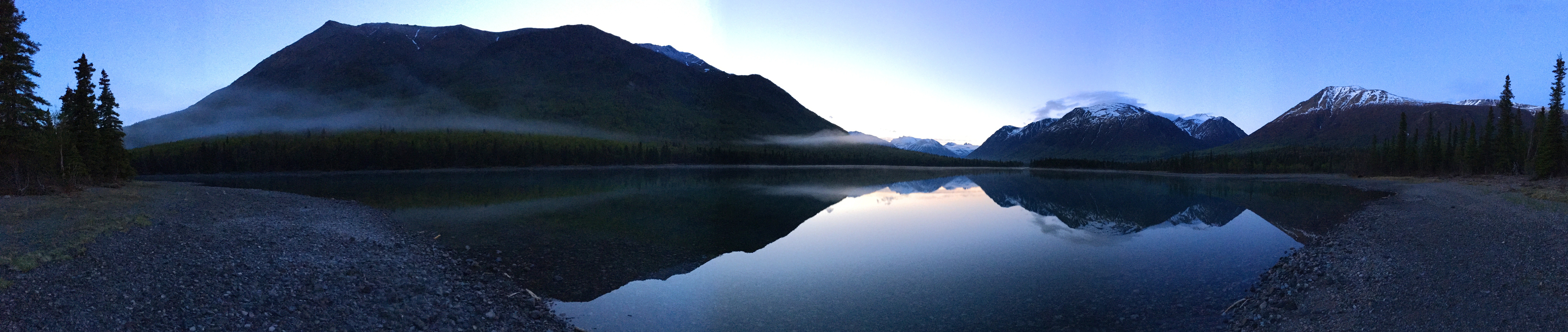 Mountains reflect in a calm blue water in morning light