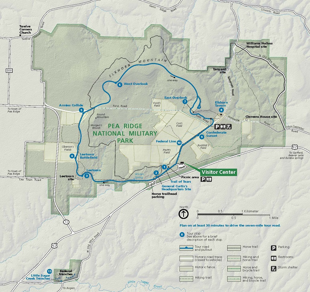 Map of Pea Ridge National Military Park in Arkansas. The park is shaded and outlined in green in the upper half of the map with the surrounding areas in a lighter green. Roads are represented by white lines, trails by dashed lines, and a tour route by a blue line.