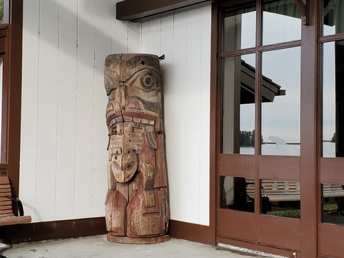 A fragment of a totem pole. Northwest Coast stylized bear holding a smaller bear to it's mouth. red and black paint on the pole is very weathered. 