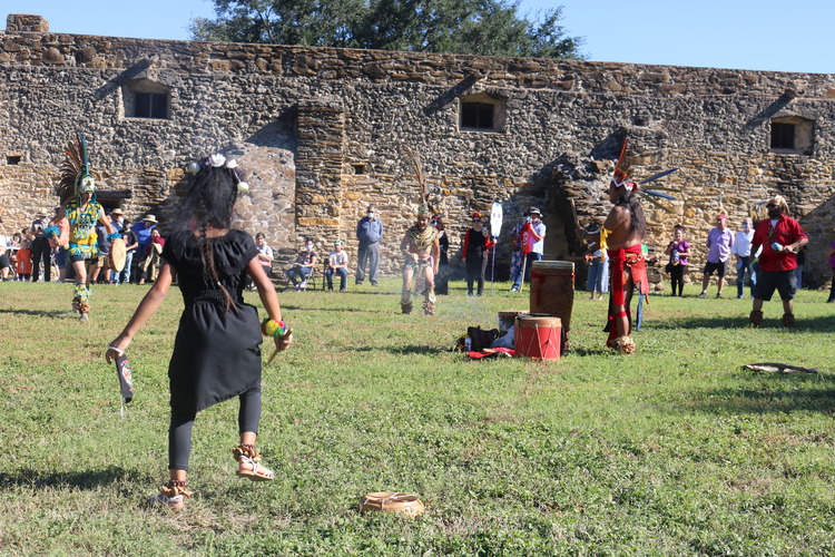 Girl dancing to the drums being played by a Native American man in the background.