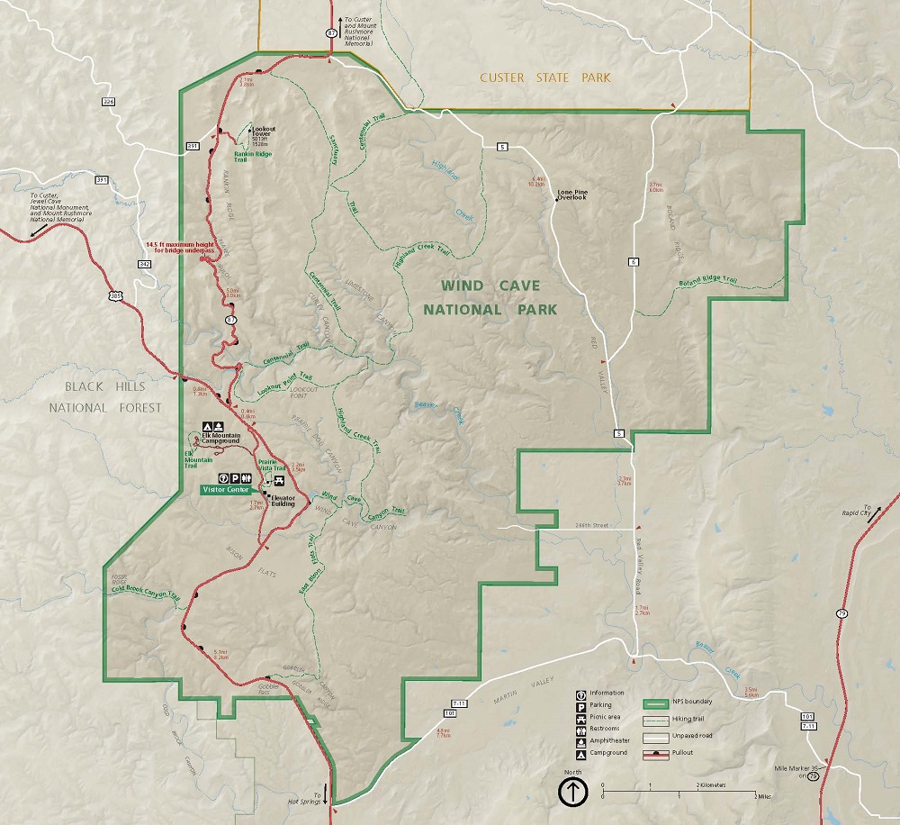 Map of Wind Cave National Park in South Dakota. The park is outlined in green and shaded a darker tan than the surrounding terrain. Paved roads and highways are represented by red lines, unpaved roads by white lines, and trails by dashed green lines.
