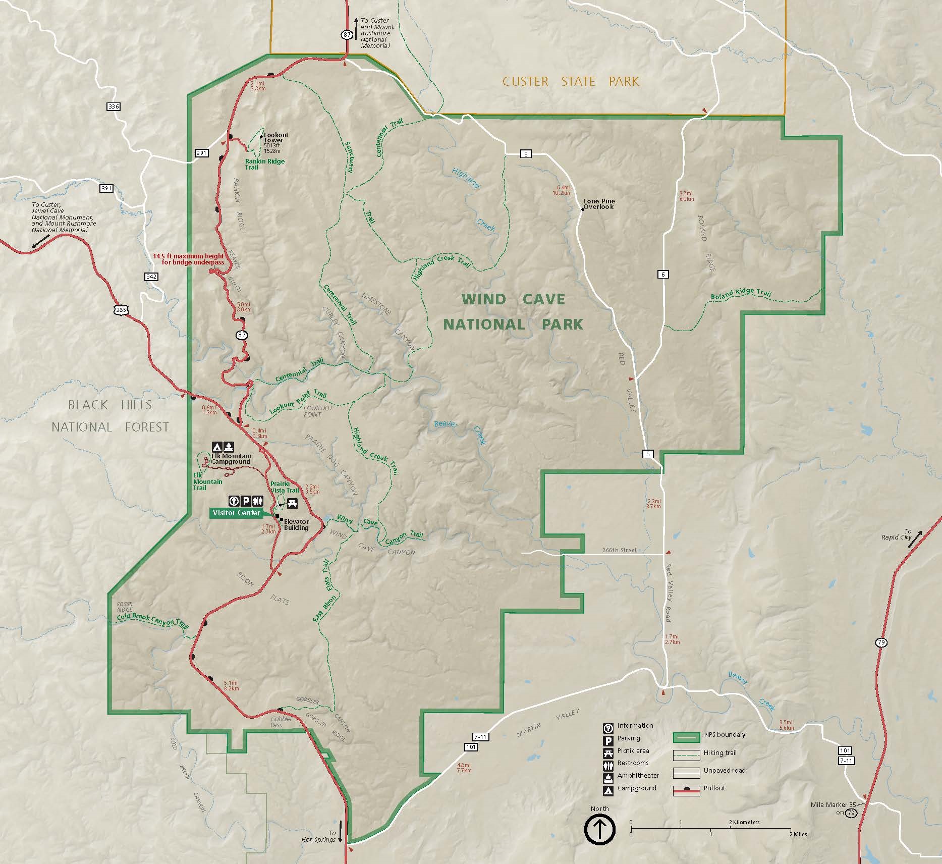 Map of Wind Cave National Park in South Dakota. The park is outlined in green and shaded a darker tan than the surrounding terrain. Paved roads and highways are represented by red lines, unpaved roads by white lines, and trails by dashed green lines.