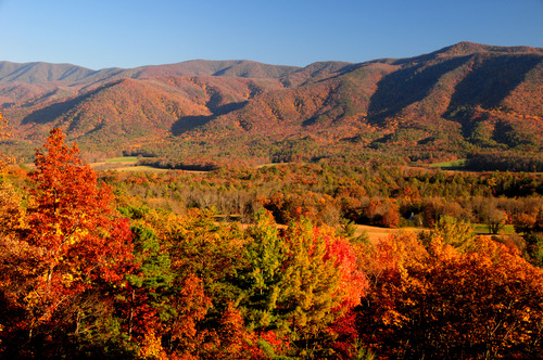 A bright fall scene over a valley with mountains surrounding.