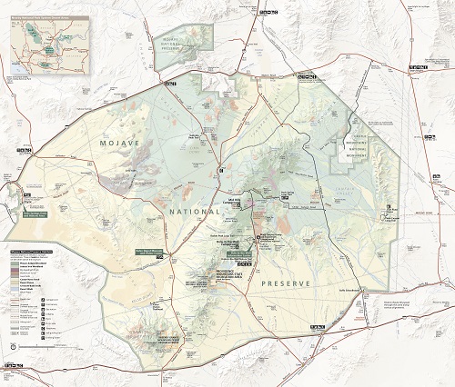 Map of Mojave National Preserve in California. The topography is shown in shades of green within the park boundary and white in the areas beyond. Dozens of trails, roads, hills, peaks, dunes, lava beds, valleys, and other sites are labeled.