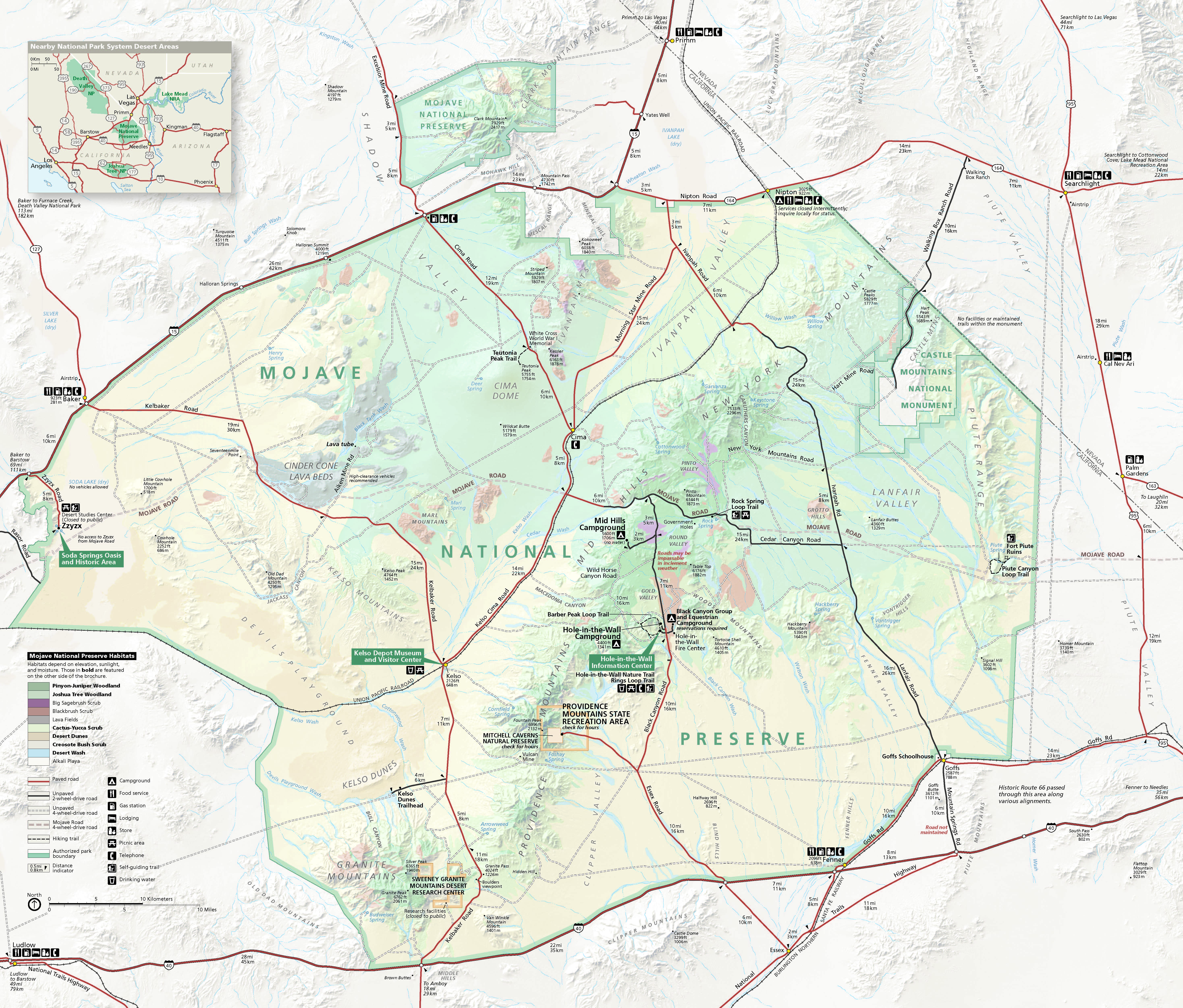 Map of Mojave National Preserve in California. The topography is shown in shades of green within the park boundary and white in the areas beyond. Dozens of trails, roads, hills, peaks, dunes, lava beds, valleys, and other sites are labeled.