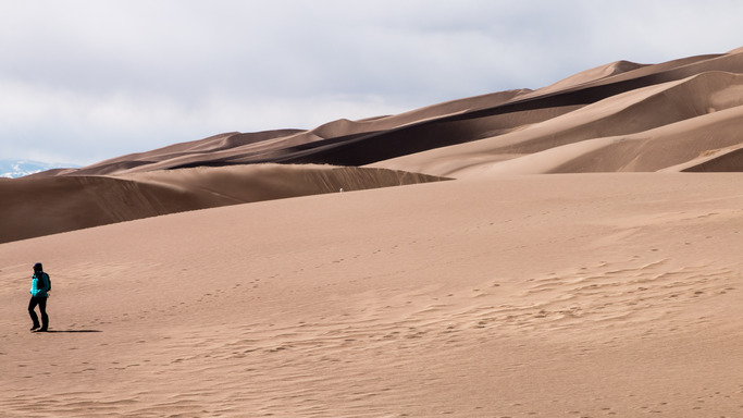 A lone park visitor walks across a large dune.
