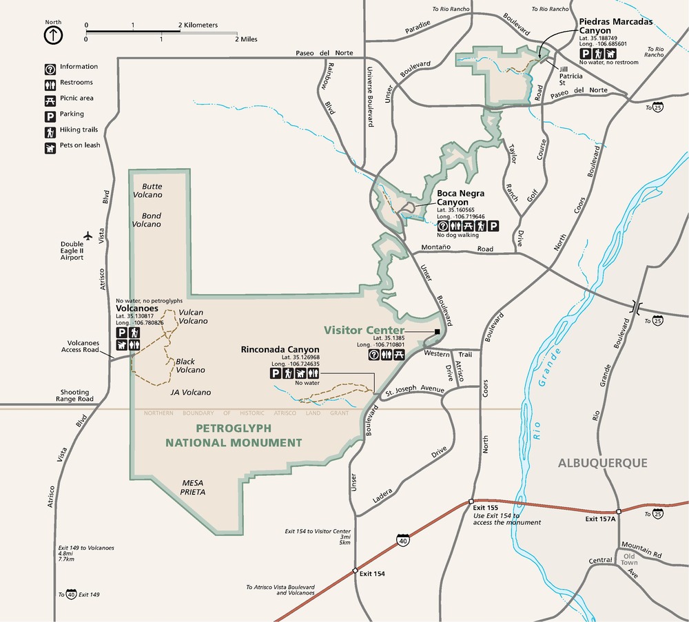 Map of Petroglyph National Monument in New Mexico. The park grounds, pale yellow with sage green borders against the white surrounding lands, are roughly triangular with a stovepipe shape that juts straight north at the northwest corner and an appendage that runs northeast like a ball of yarn.